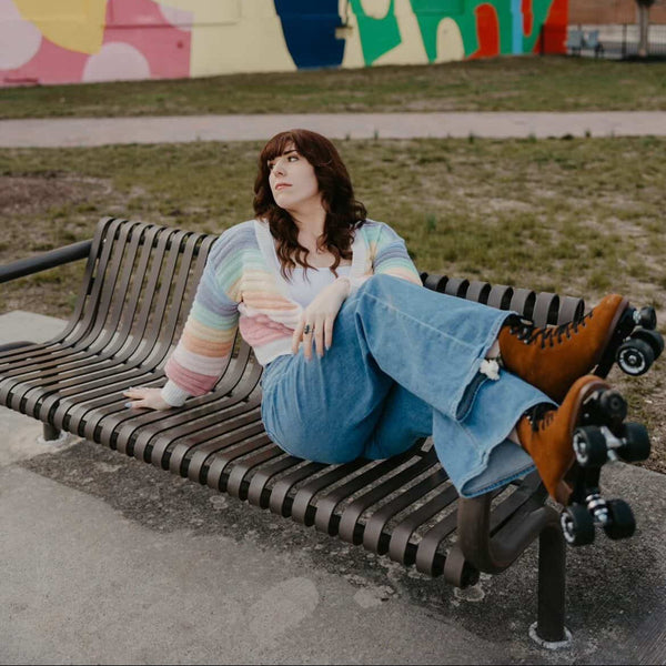 Person sitting on a bench wearing brown roller skates in front of a colorful mural